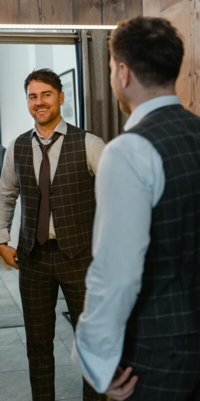 A man in a designer suit smiles while adjusting his tie in a stylish tailor shop.