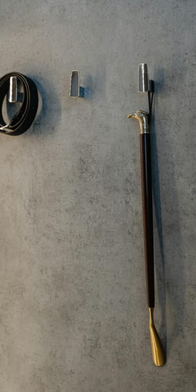 A sophisticated display of a belt and walking cane hanging on a textured wall.