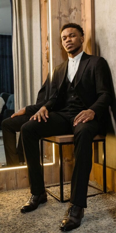 A stylish man in a suit sits in a tailor shop fitting room, embodying elegance and sophistication.